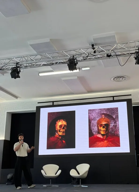 Muhju speaks into a microphone onstage, with two of his skull artworks on the screen behind him.