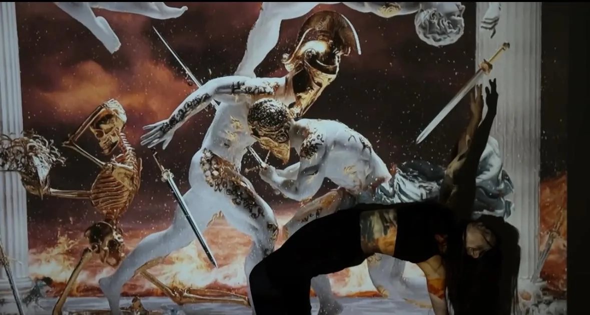A performer bends backwards before a projected battle scene with a skeleton and white winged figures.