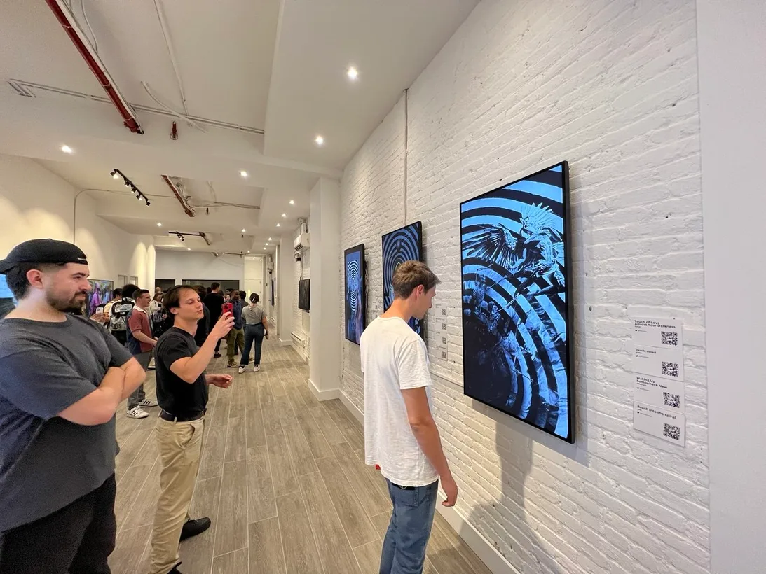 Visitors view screens displaying blue swirling artworks in a long white brick gallery.