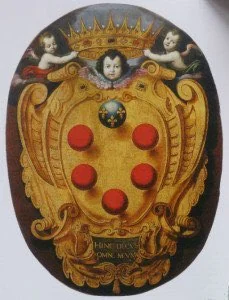 An oval painted golden Medici shield beneath a crown, with two cherub heads and an inscription below.