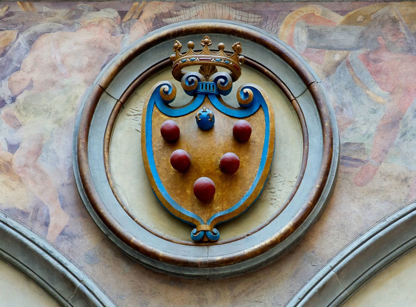 A crowned Medici shield in a carved stone roundel set into a frescoed vault.